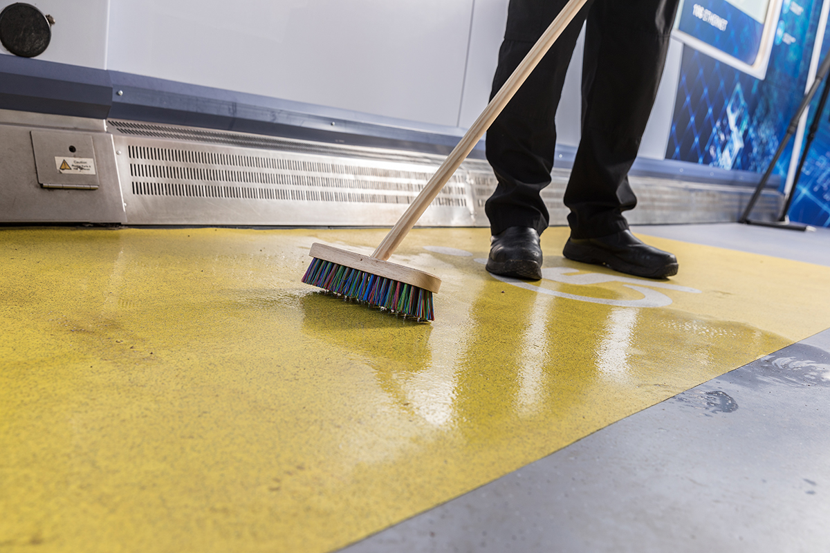 A bristle brush being used to agitate cleaner on Altro Transflor Tungsten in safety yellow