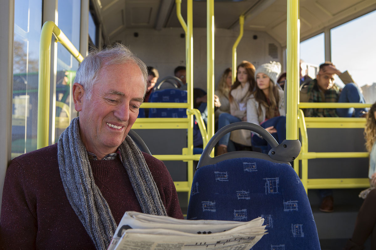 A smiling elderly man reading a newspaper on his local bus service